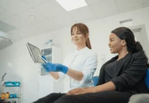 The Role of Digital Transformation in Health Care Marketing A smiling health care professional wearing blue gloves shows a patient medical information on a tablet in a clinical setting