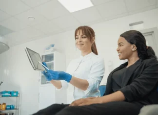 The Role of Digital Transformation in Health Care Marketing A smiling health care professional wearing blue gloves shows a patient medical information on a tablet in a clinical setting