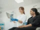The Role of Digital Transformation in Health Care Marketing A smiling health care professional wearing blue gloves shows a patient medical information on a tablet in a clinical setting