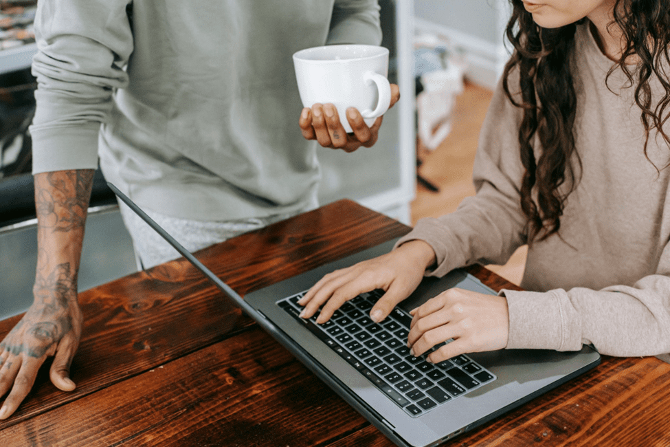 A patient browsing a healthcare website while another person, holding a coffee mug, stands nearby.