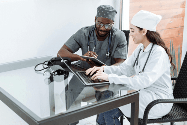 Two healthcare professionals discussing patient data on a laptop, collaborating in a modern clinic setting.
